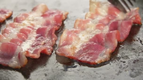 Gros plan de bandes de délicieux bacon retournant sur la surface plate du gril — Video