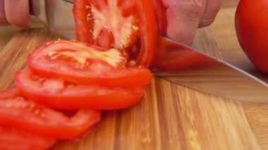 Kırmızı olgun bir domatesi dilimlere ayıran ellerin yakın çekimi.