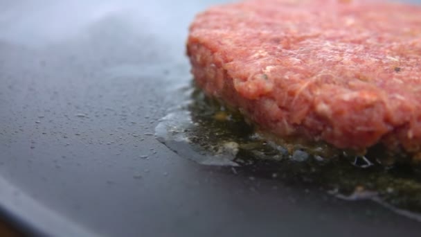 Costeleta de carne crua para um hambúrguer está fritando na superfície plana da grelha — Vídeo de Stock