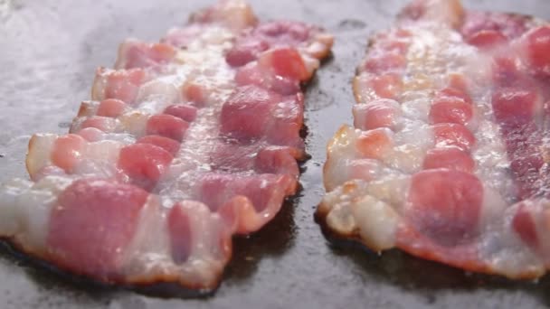 Close-up of strips of delicious bacon roasting on the flat grill surface — Stock Video