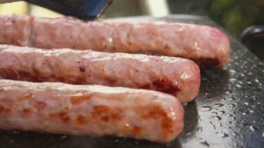 Düz ızgarada spatulayla çevrilmiş leziz kızarmış sosislerin yakın çekimi.