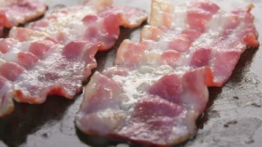 Düz ızgara yüzeyinde pişen lezzetli domuz pastırması şeritlerinin süper yakın çekimi.