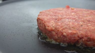 Hamburger için çiğ biftek ızgarada kızarıyor ve cızırdıyor. 