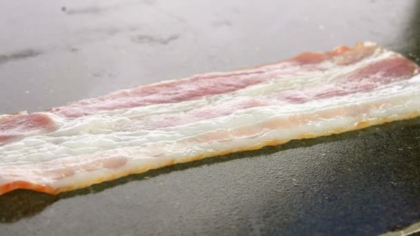 Gros plan de délicieuses lanières de bacon frites prises sur la surface plane du gril — Video