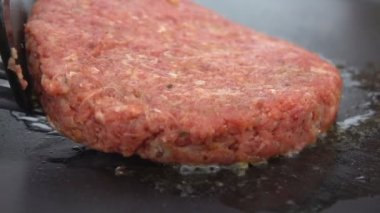 Hamburger için çiğ sığır pirzolası düz ızgara yüzeyine konur.