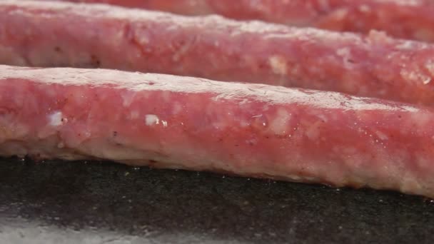 Крупный план сырых колбас, жарящихся на плоском каменном гриле — стоковое видео