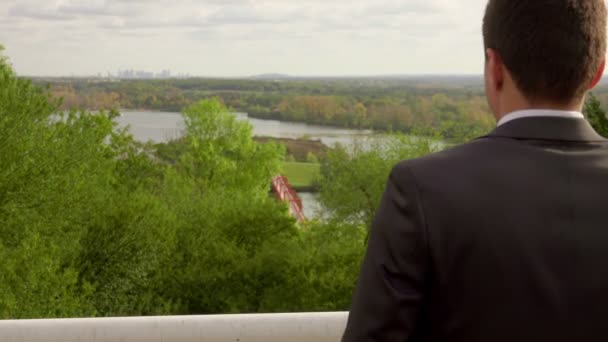 Un homme d'affaires prospère regarde la vue sur le parc verdoyant avec un lac — Video