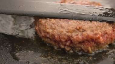 Hamburger için sulu sığır pirzolası. Düz ızgarada spatulayla eziliyor.
