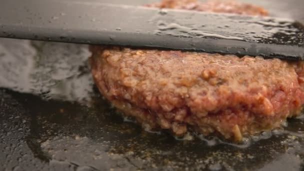 Sappig rundvlees voor een hamburger wordt geperst met een spatel naar de platte grill — Stockvideo