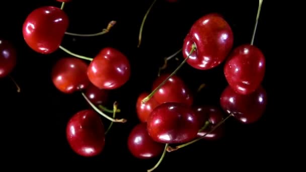 Смачні соковиті червоні вишні підстрибують на чорному тлі — стокове відео