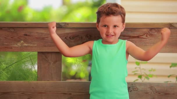 El niño bronceado está mostrando músculos bíceps. — Vídeos de Stock