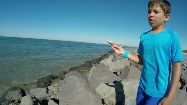 Щасливий хлопчик грає з моделлю літака на фоні моря — стокове відео