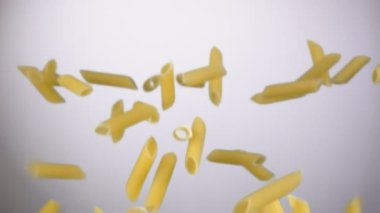 Kuru çiğ makarna penne yukarı uçuyor ve beyaz arka planda düşüyor.