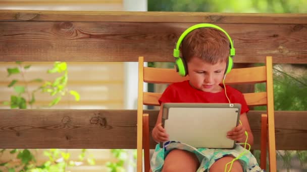 Der kleine Junge mit Kopfhörer hört Musik auf dem digitalen Tablet — Stockvideo