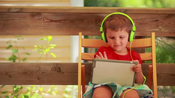 The little boy in green earphones listens to music on the digital tablet — Stock Video