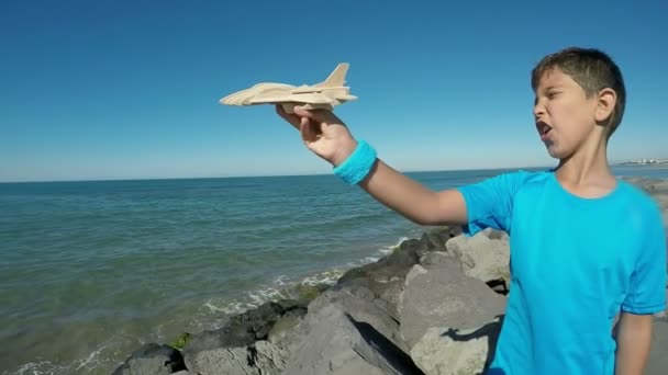 Een vrolijke jongen speelt met een vliegtuig model op de achtergrond helder blauwe lucht — Stockvideo