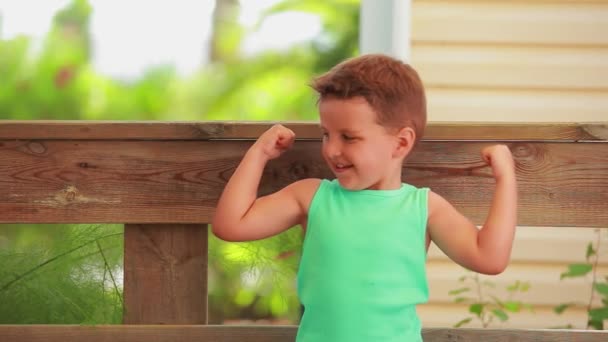 Malý veselý chlapec v zeleném tričku ukazuje svaly bicepsu — Stock video