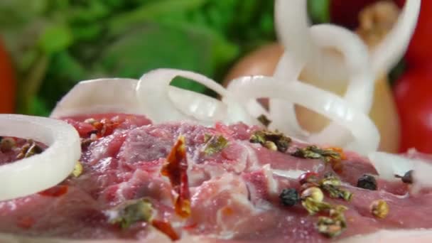 Anillos de cebolla están cayendo sobre la carne cruda espolvoreada con pimienta y especias — Vídeo de stock