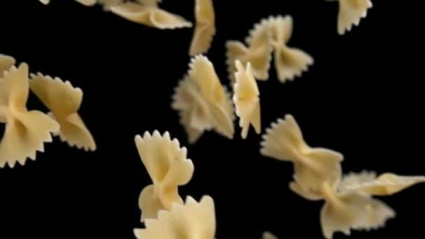 Trockene Pasta Farfalle fliegt diagonal auf schwarzem Hintergrund — Stockvideo