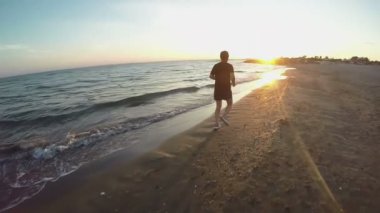 Gün batımında deniz kıyısında koşan bir adamın silüeti.