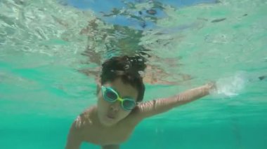 Yüzme gözlüklü ve mayolu bir çocuk suyun altında kıvrılıyor.