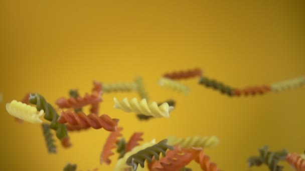 Dry colored pasta fusilli flying up and rotating on a yellow background — Stock Video