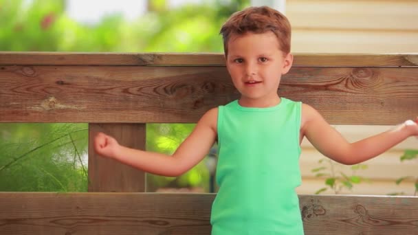 Den lilla glada pojken i en grön t-shirt visar muskler — Stockvideo