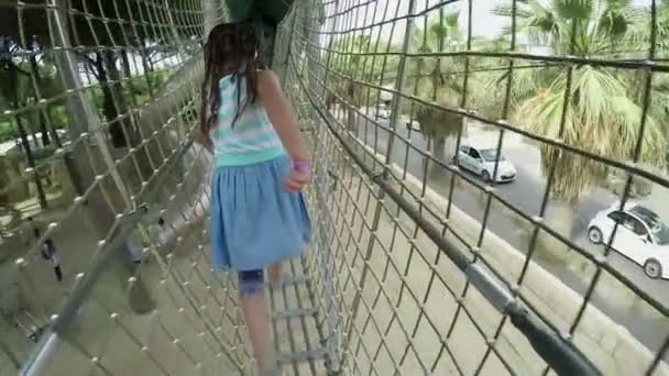 Вид сзади на девушку, идущую по высокому безопасному мосту на детской площадке — стоковое видео