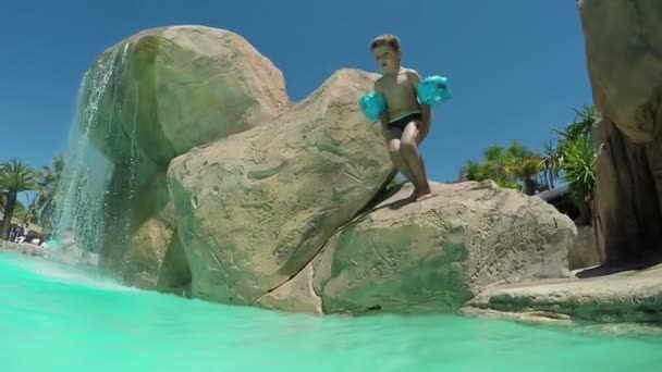 Мальчик прыгает со скалы в аквапарке и ныряет в бассейн — стоковое видео