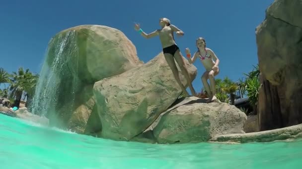 Menino e menina felizes estão pulando do penhasco artificial no parque aquático — Vídeo de Stock