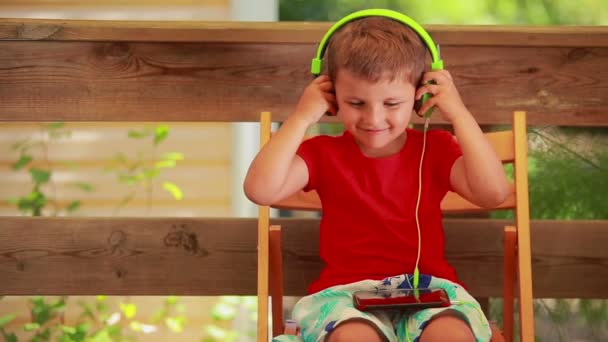 Het jongetje zet een groene koptelefoon op en luistert naar muziek. — Stockvideo