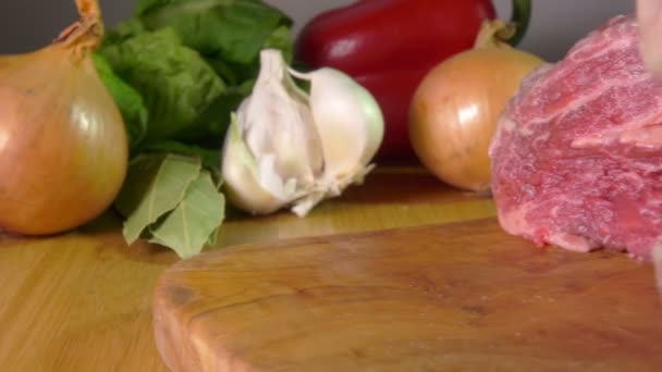 Кусок сырого мяса падает на доску на фоне чеснока — стоковое видео