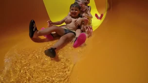 Gruppo di bambini felici in sella a uno scivolo arancione in un parco acquatico — Video Stock