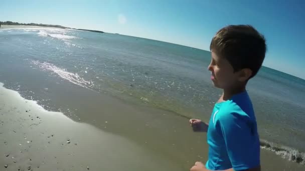 The cheerful boy is running along the coastline on a background of the sea — Stock Video