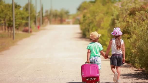Chłopiec i dziewczyna w kapeluszach idą ręka w rękę wzdłuż drogi. — Wideo stockowe