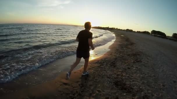 El hombre está corriendo en la hermosa orilla del mar al atardecer — Vídeos de Stock