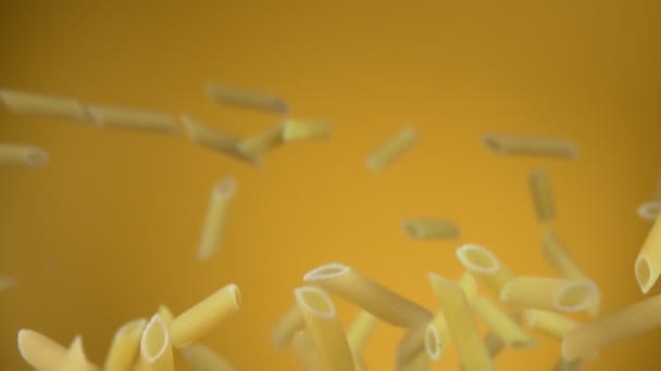 Pasta cruda seca penne volando arriba y abajo sobre un fondo amarillo — Vídeos de Stock