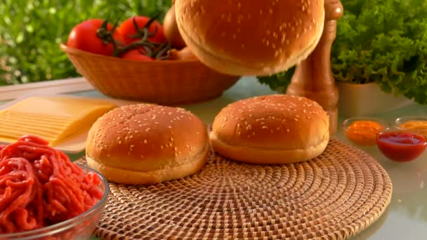 Cesam-Brötchen fällt neben den Zutaten für Cheeseburger auf den Tisch — Stockvideo