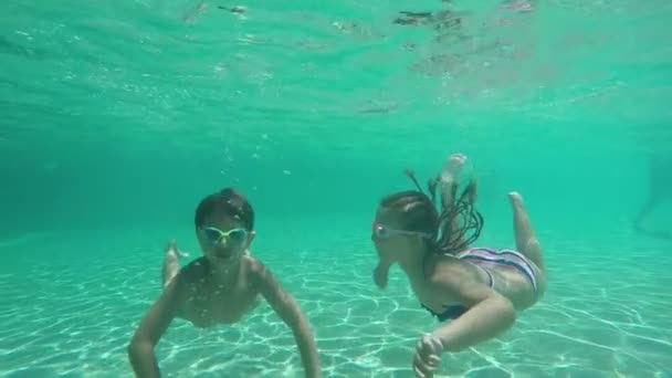 Fiú és lány úszószemüvegben búvárkodnak és úsznak a víz alatt a medencében. — Stock videók