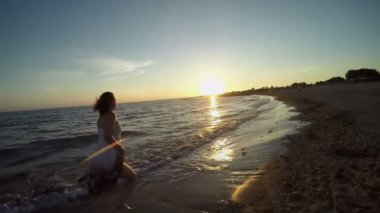 Sahilde gün batımına doğru koşan genç bir kadının silüeti.