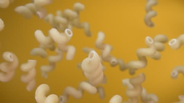 Trockene Pasta cellentani fliegt diagonal auf gelbem Hintergrund — Stockvideo