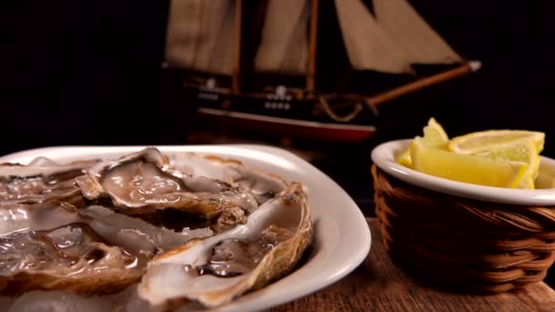 Kézzel vesz friss osztrigát egy fehér tányérról a modell hajó hátterében. — Stock videók