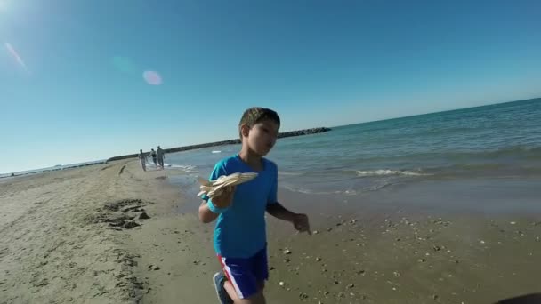 El niño alegre está corriendo por la playa de arena con un modelo de avión — Vídeos de Stock