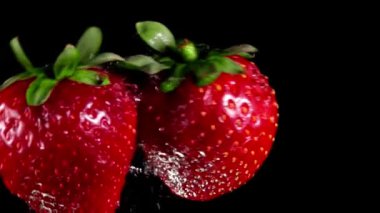 Siyah arka planda iki büyük çilek çarpışıyor.