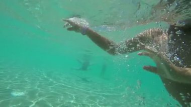 Yüzme gözlüklü çocuk yüzüyor ve su altında jestler gösteriyor. 