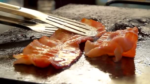 Primo piano di strisce di pancetta che girano con pinze metalliche sulla superficie della griglia piana — Video Stock