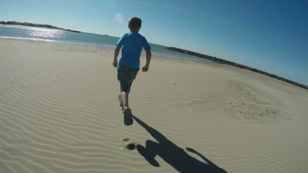 El niño alegre está corriendo por la playa en un fondo del mar — Vídeos de Stock