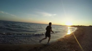 Aktif bir adam gün batımında deniz kıyısında koşuyor.