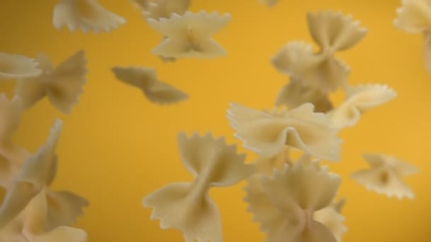 Pâtes sèches Farfalle tombe en diagonale sur un fond jaune — Video