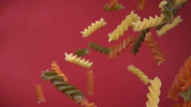 Dry colored pasta fusili flying diagonally on a wine red background — Stock Video